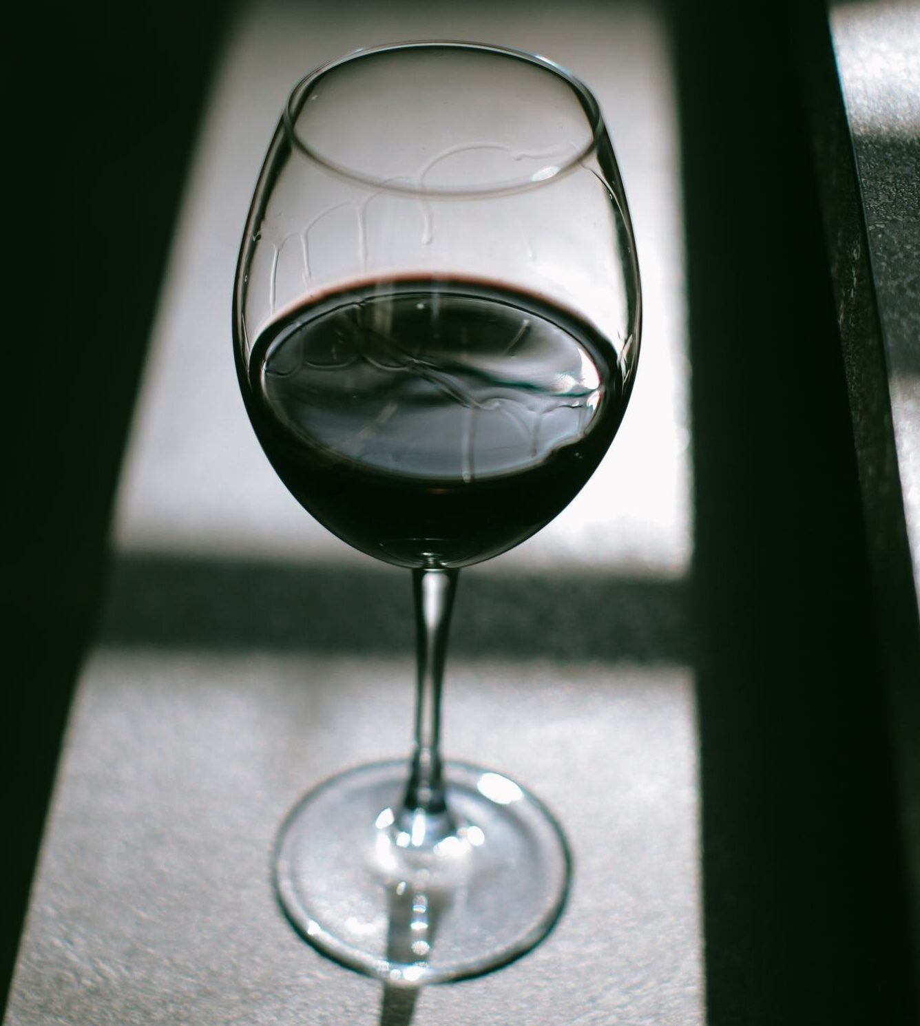 A glass of red wine casting intriguing shadows on a textured surface.